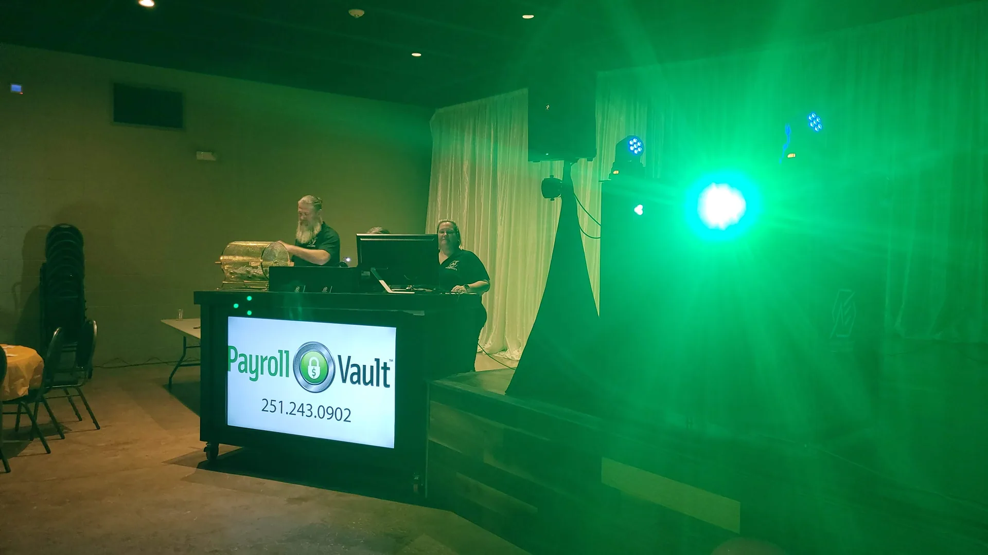 A Payroll Vault sponsor slide on the booth screen, the room washed in green stage lighting.
