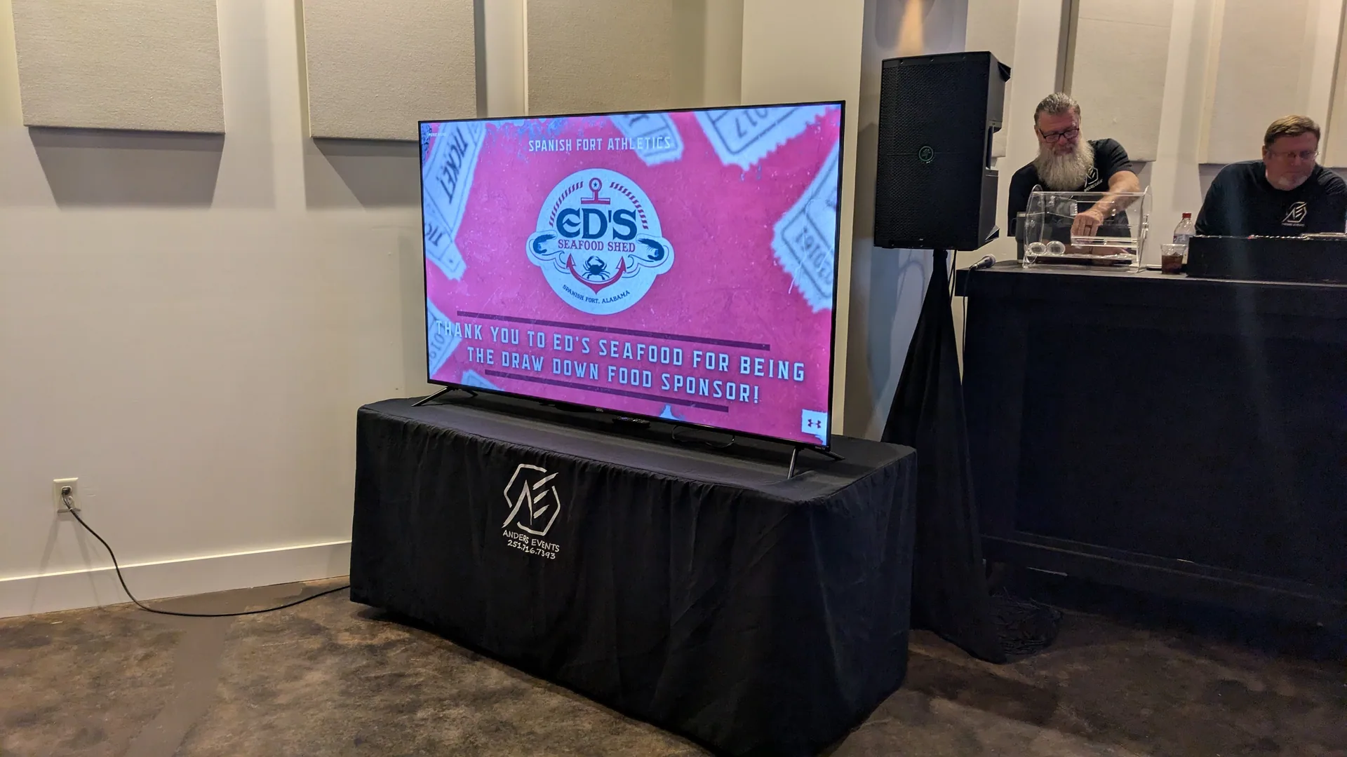 A 65-inch screen on a branded Anders Events skirt displaying a sponsor slide thanking Ed's Seafood Shed for sponsoring the draw down.