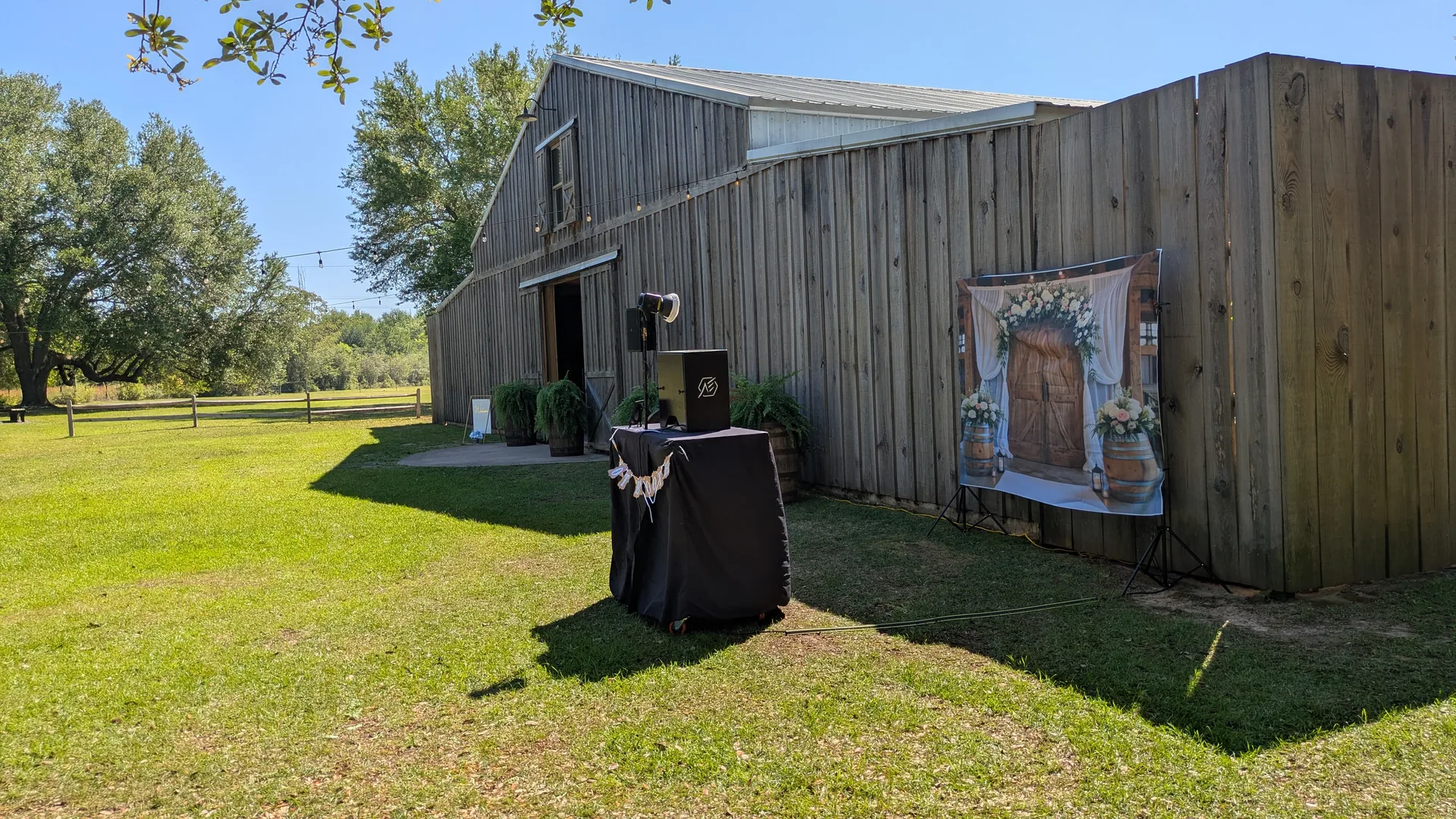 The photo booth and a floral backdrop set up on the grass beside a barn venue, with no power cable running to either.
