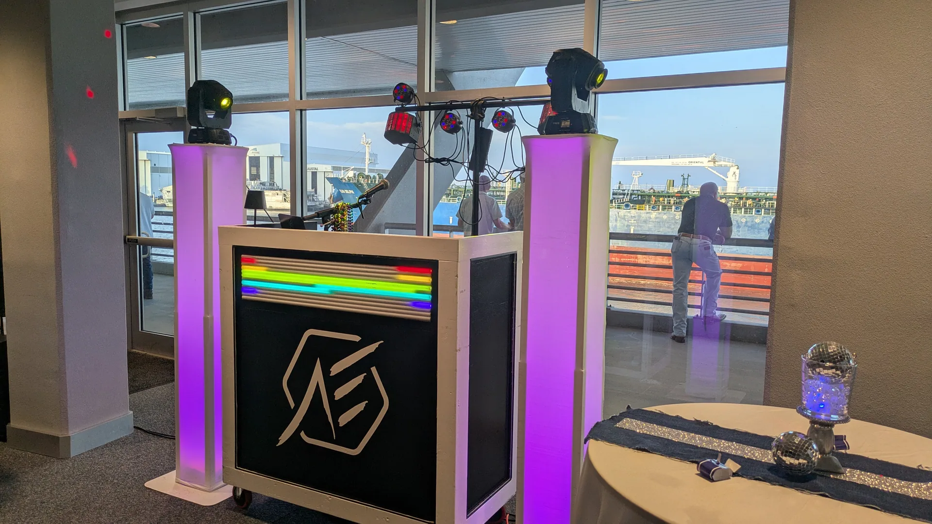 DJ booth with an RGB LED matrix across its face and moving-head lights mounted on lit columns.